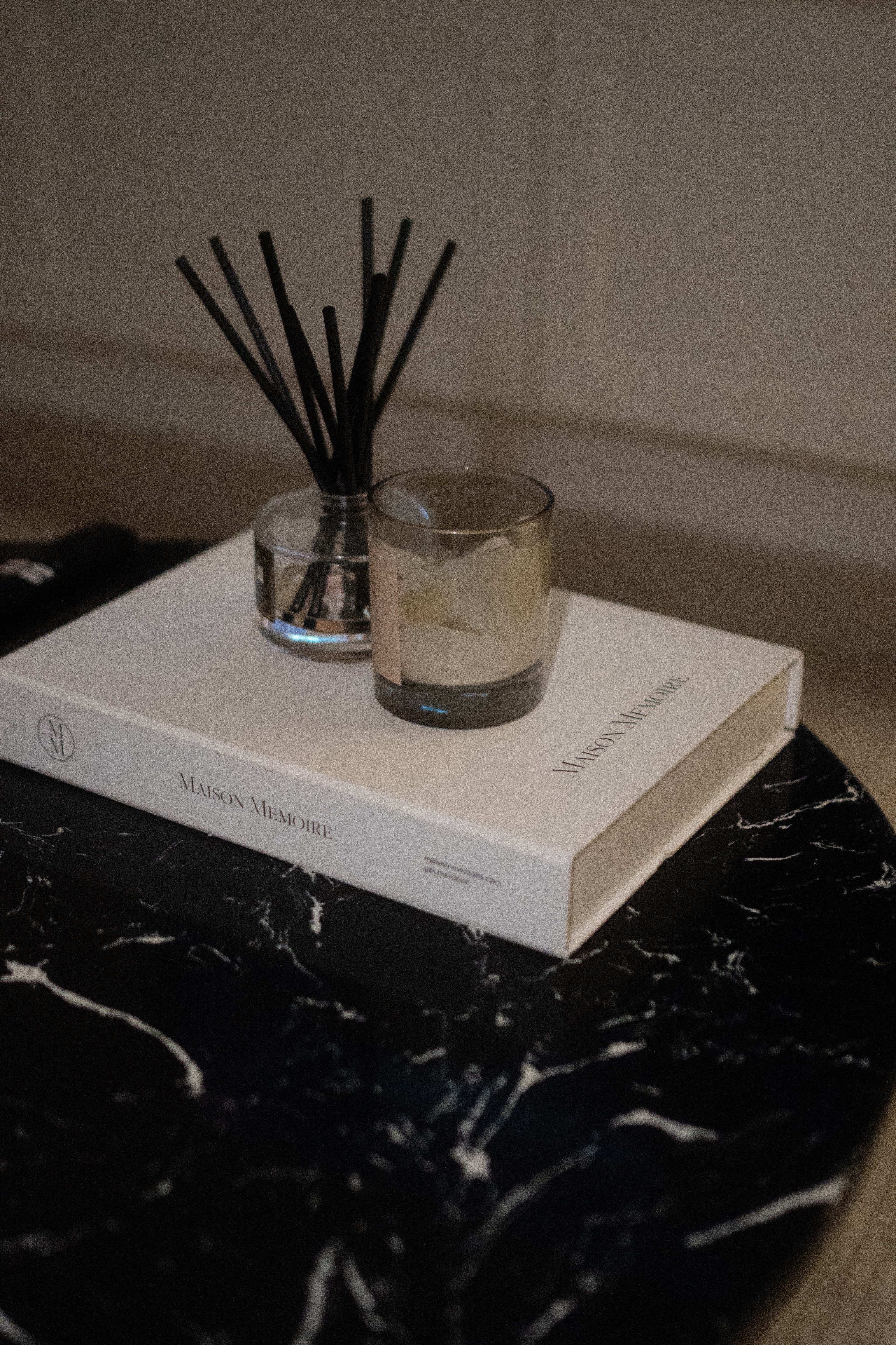An ivory Maison Mémoire book with a candle and reed diffuser on a dark marble table